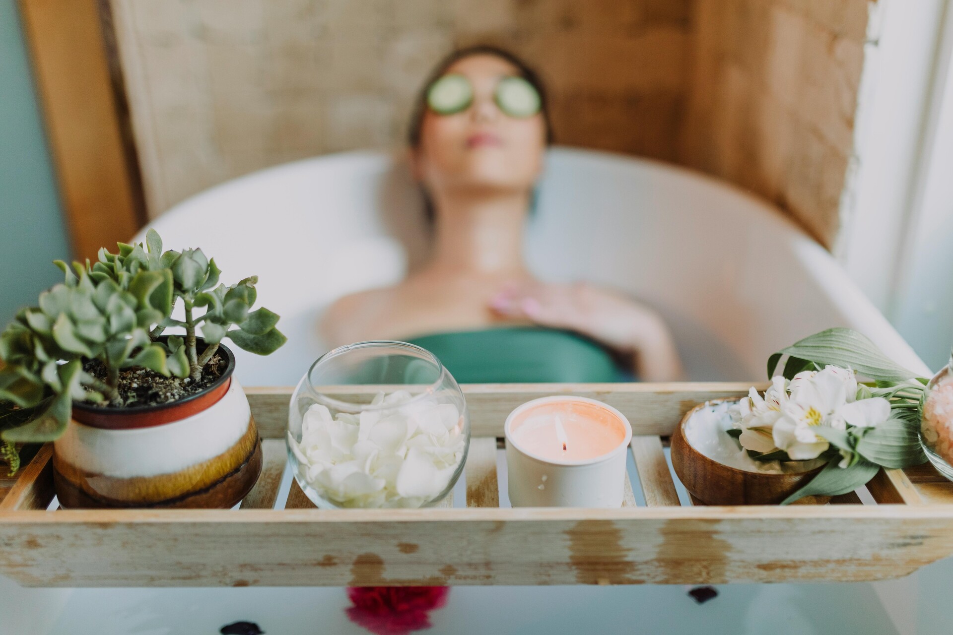 Mujer relajándose en una bañera con una vela y plantas, disfrutando de una serena experiencia de spa.