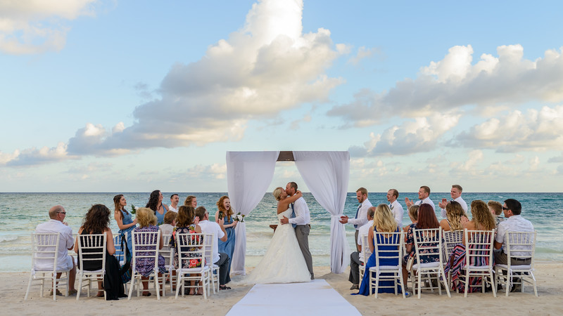 a man and woman kissing at a beach wedding