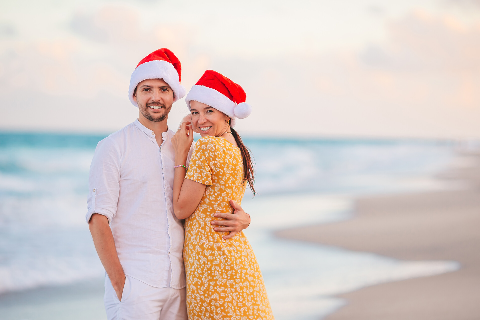 a man and woman wearing santa hats on a beach