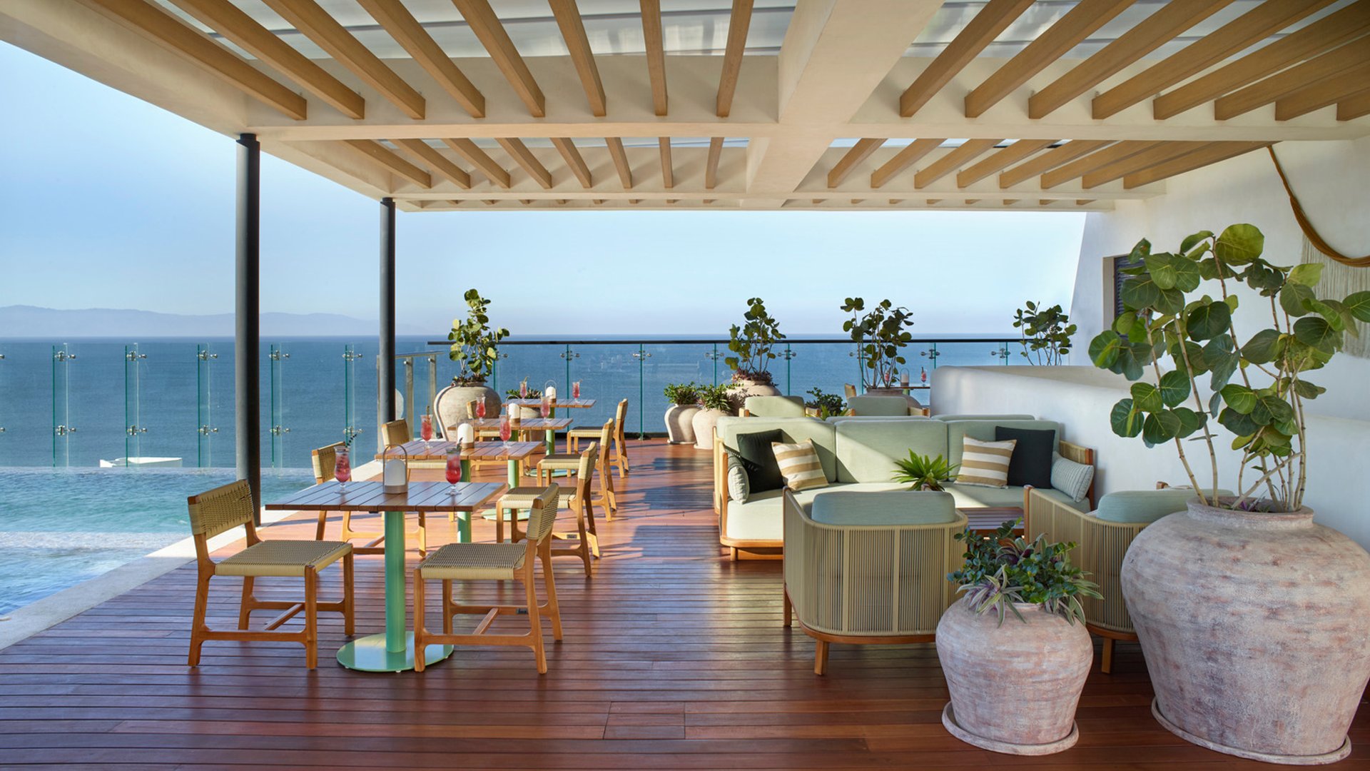 Outdoor terrace with wooden flooring, modern wicker furniture, planters, and ocean view.